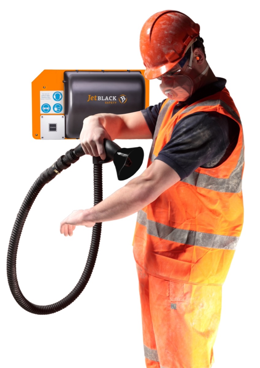 Man in PPE using the wall mounted JetBlack Safety Personnel Cleaning Station to blow dust off his arm